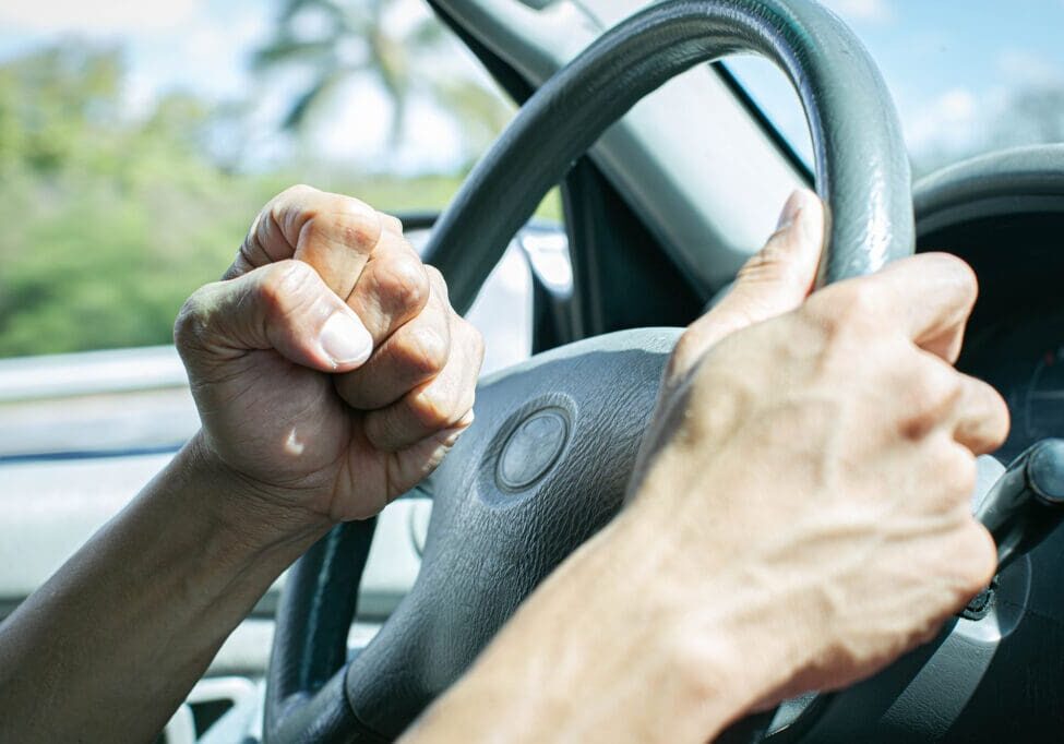 A man behind the steering wheel angry at other drivers banging on his horn in anger.